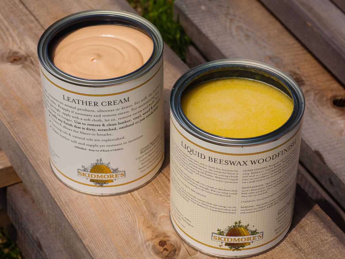 Open cans of Skidmore’s Leather Cream and Liquid Beeswax Woodfinish on a weathered wood bench
